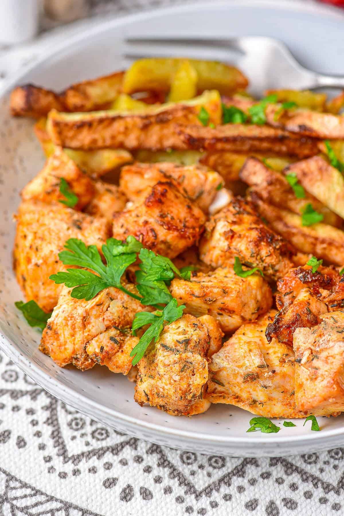 A close-up of air fryer chicken and potatoes served on a plate with fresh parsley and cherry tomatoes.