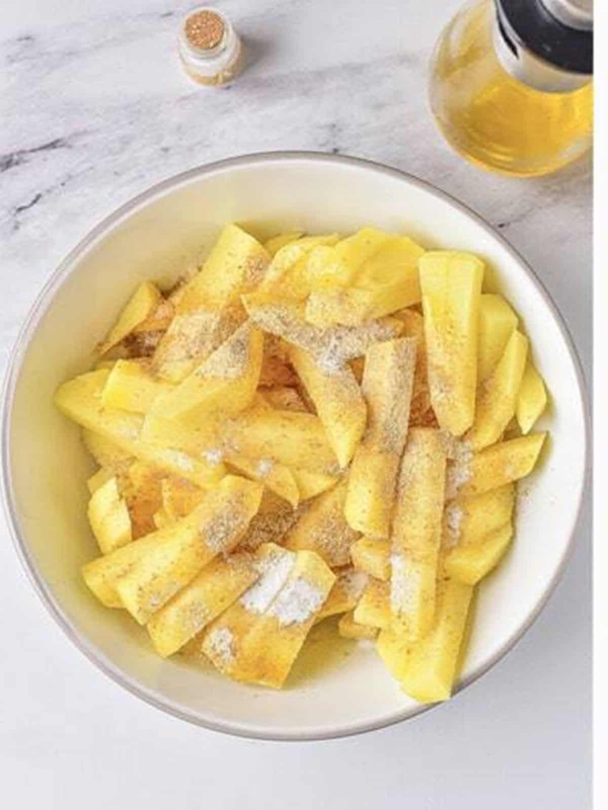 Yukon gold potato strips tossed with salt, spices, and olive oil in a bowl for air fryer chicken and potatoes.