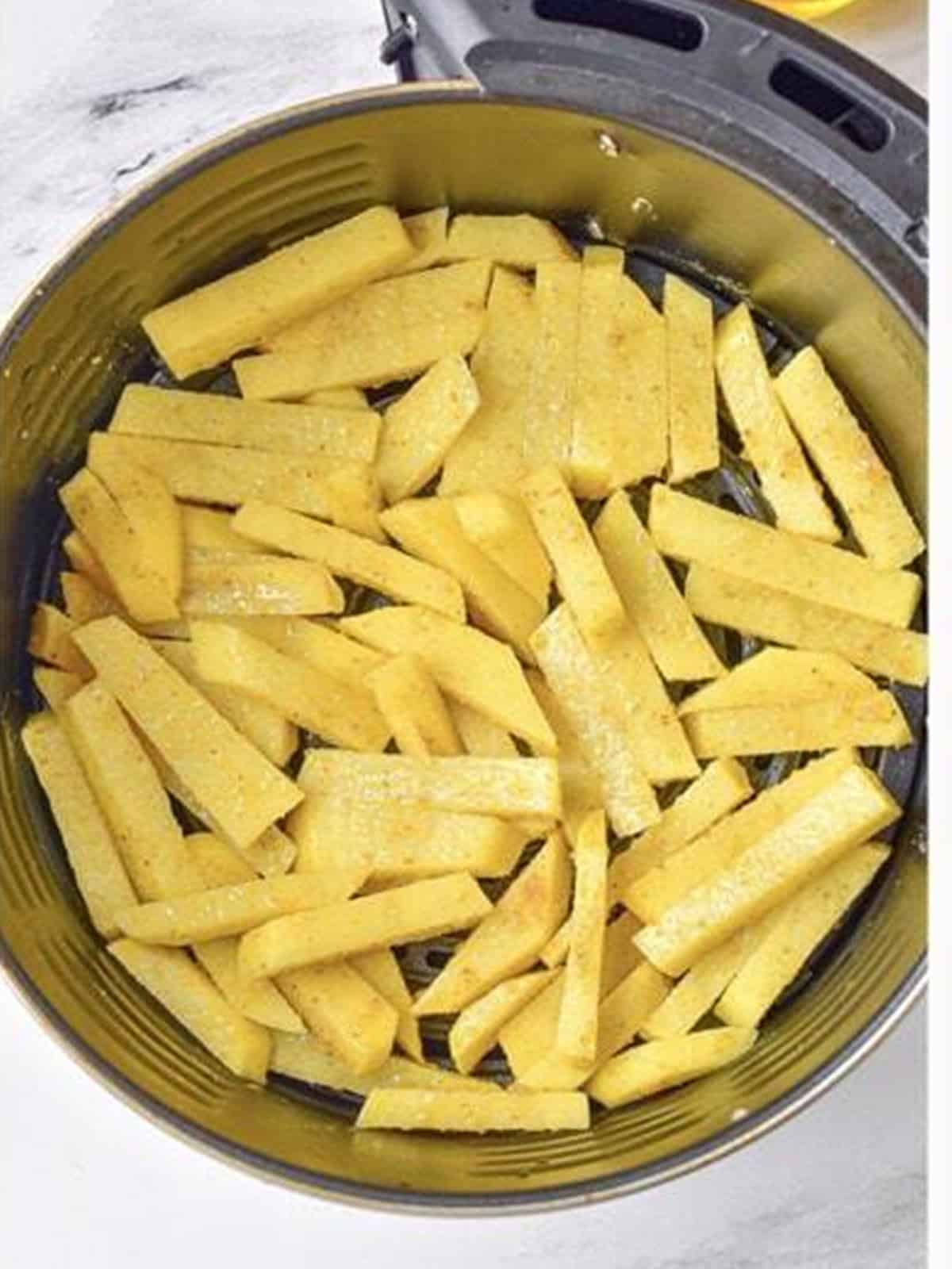 Seasoned potato strips arranged in a single layer in the air fryer basket.