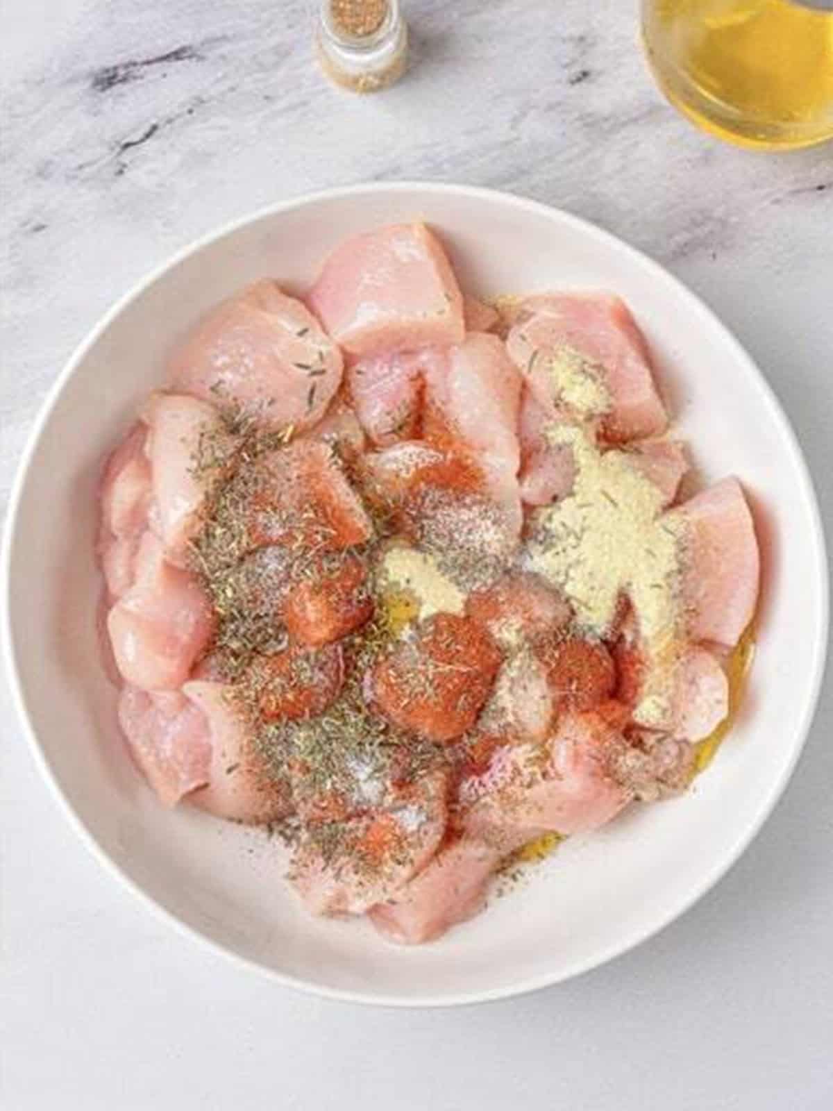 Diced chicken breast in a bowl topped with salt, paprika, and spices for air fryer chicken and potatoes.