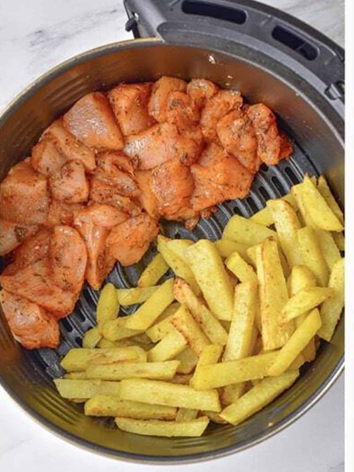 Seasoned chicken and potatoes arranged side by side in the air fryer basket.