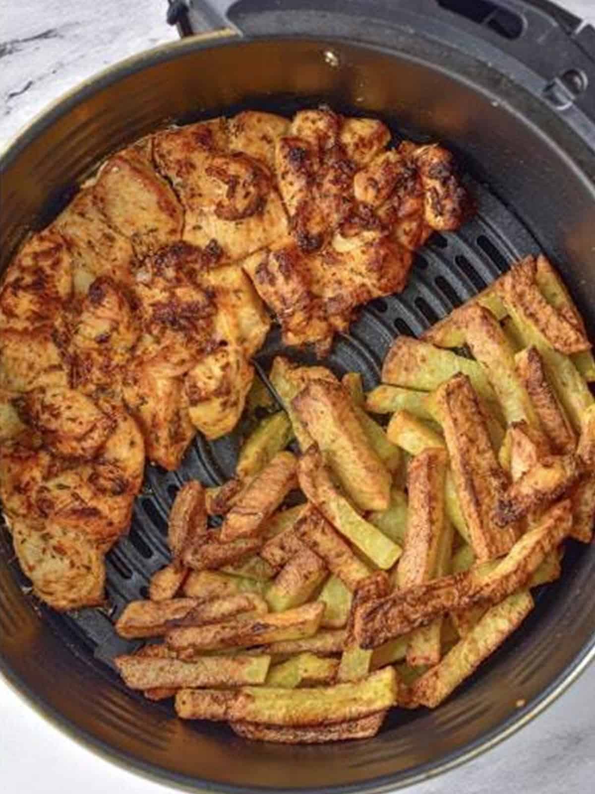 Golden browned air fryer chicken and potatoes finished cooking in the basket.