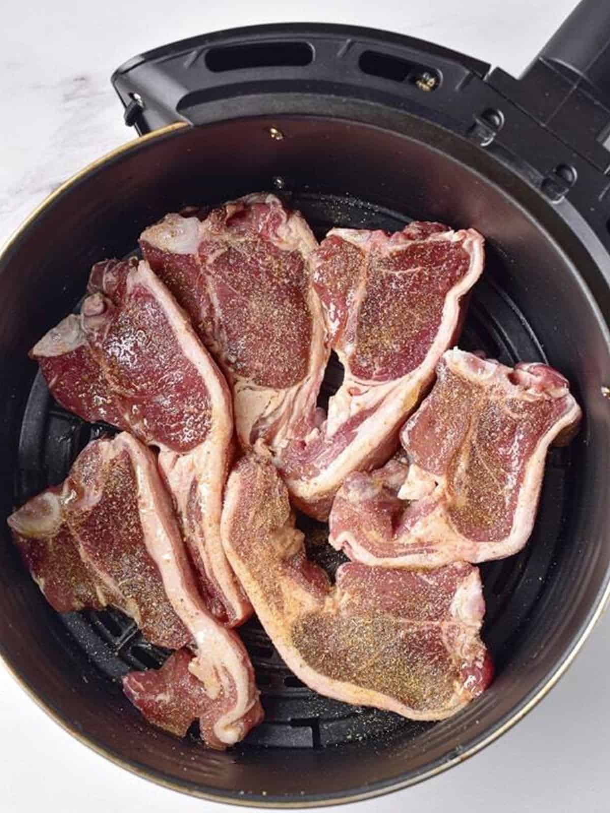 Seasoned lamb chops arranged in an air fryer basket before cooking.