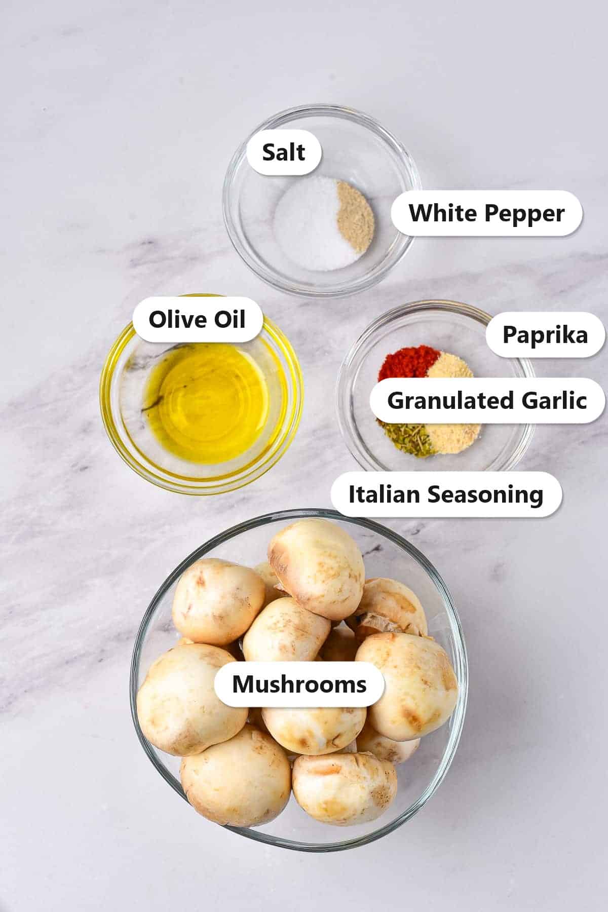 Labeled ingredients to make air fryer mushrooms including button mushrooms, olive oil, salt, white pepper, paprika, granulated garlic, and Italian seasoning