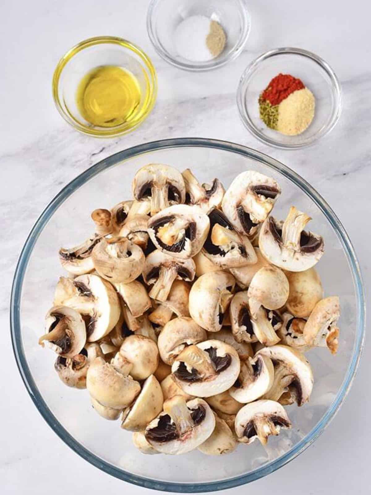 Cut button mushrooms in a large glass bowl with oil and seasonings ready to add