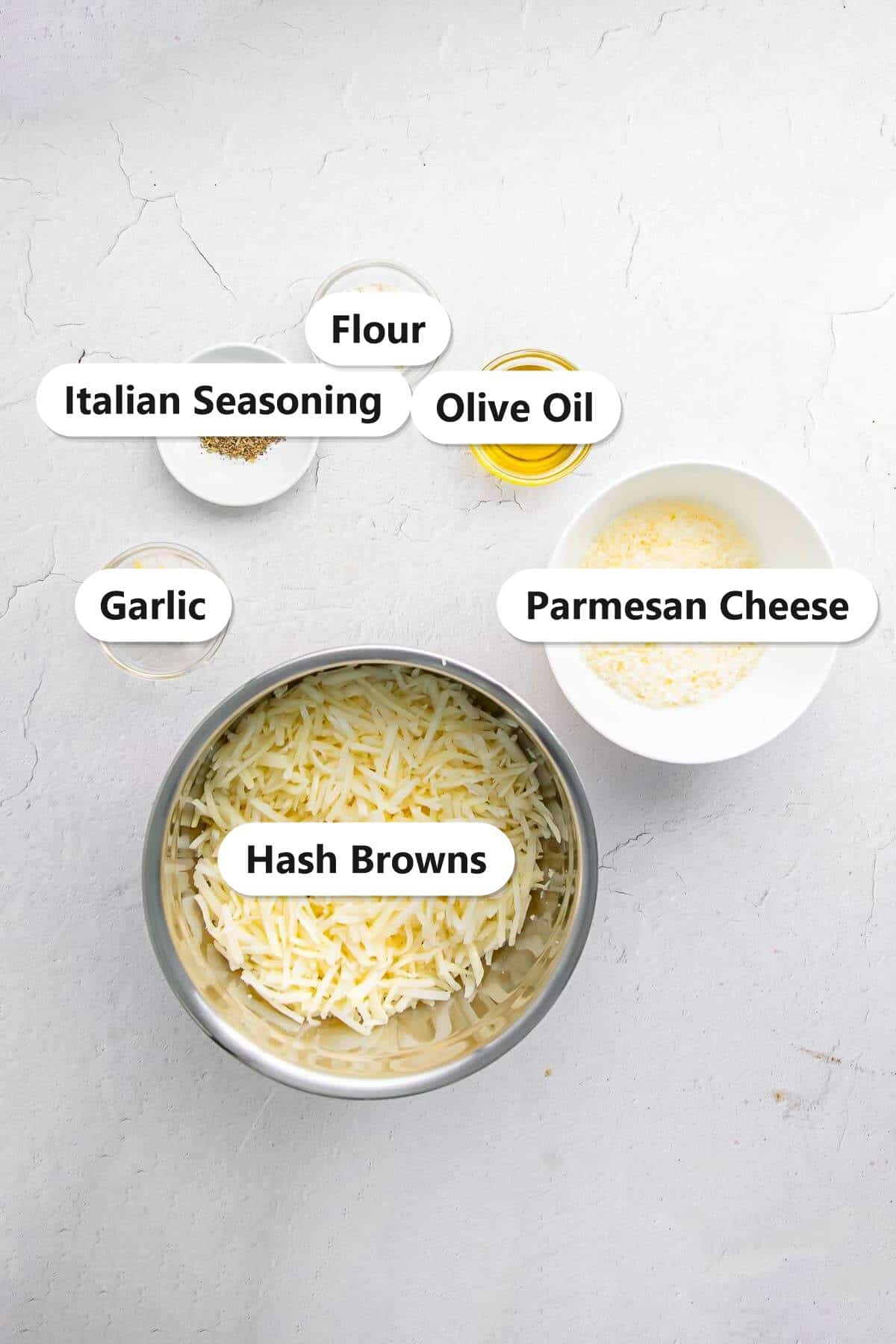 Labeled ingredients to make air fryer tater tots including shredded hash browns, parmesan cheese, olive oil, flour, garlic, and Italian seasoning.