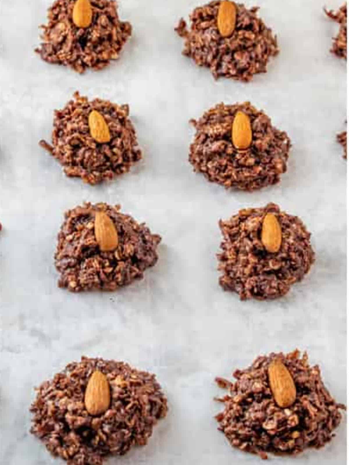 Scooped almond joy cookies on parchment paper each topped with a whole almond