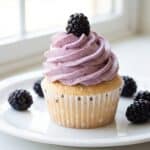 An angel food cupcake topped with a swirl of pale purple blackberry buttercream and a fresh blackberry.