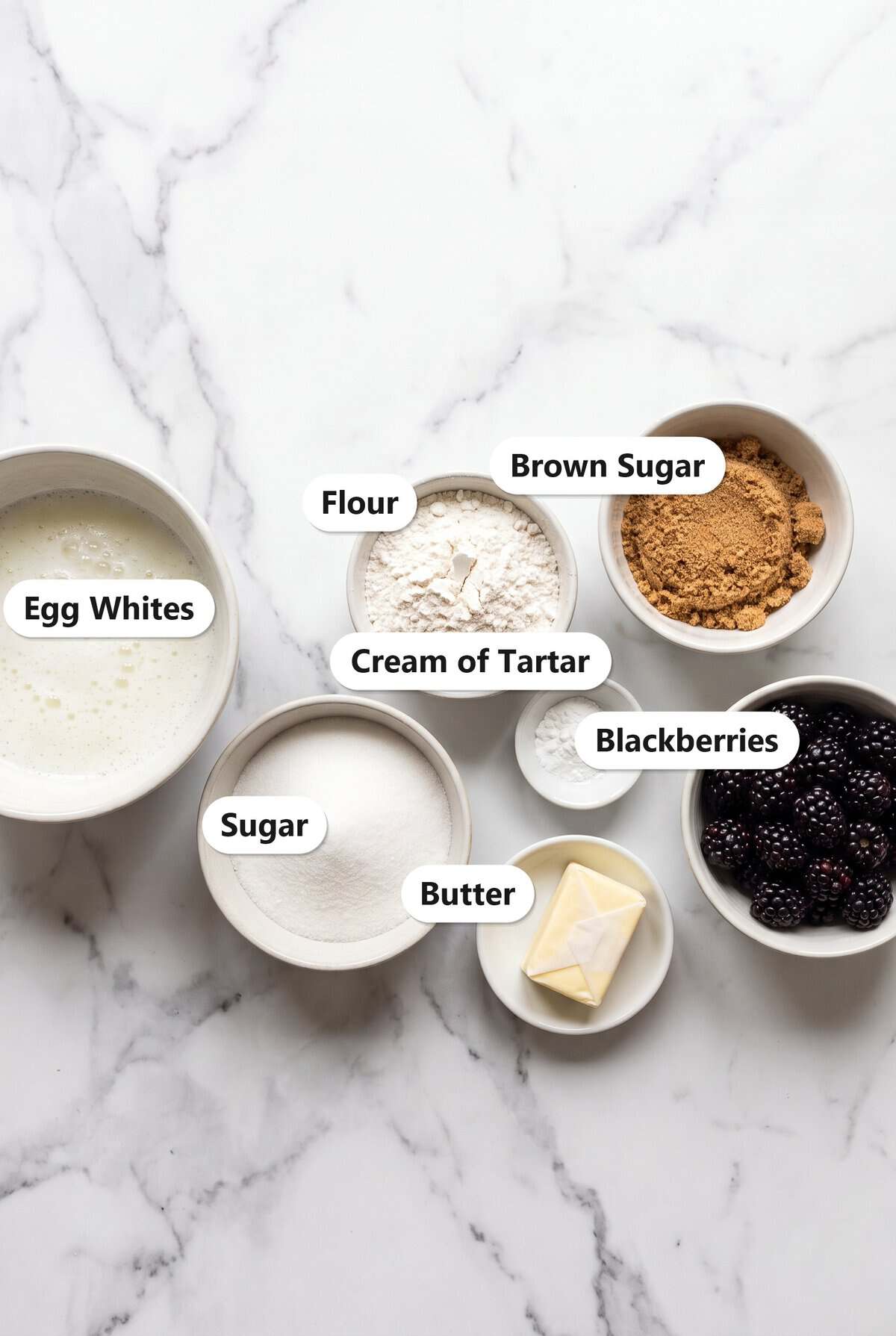 Labeled ingredients to make angel food cupcakes with blackberry frosting including egg whites, flour, sugar, brown sugar, cream of tartar, butter, and blackberries.