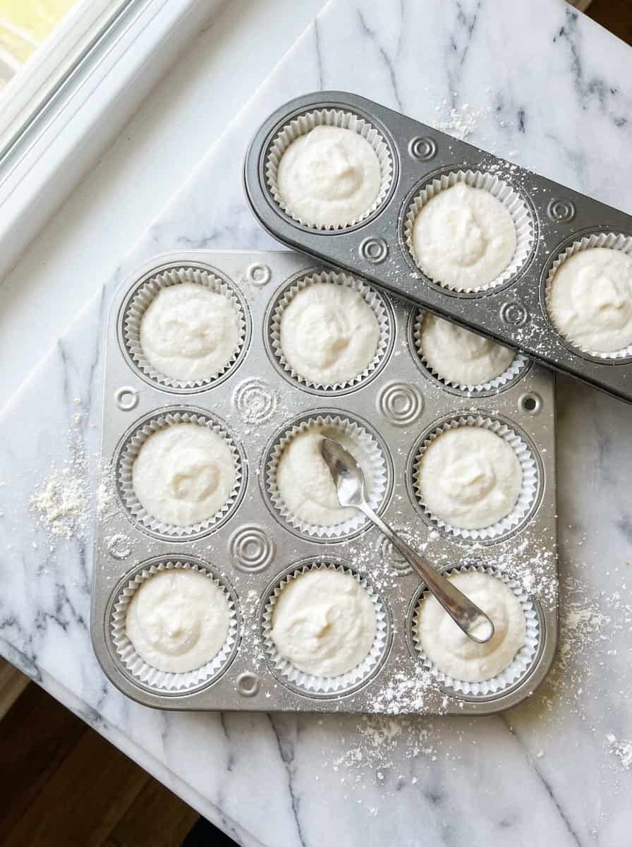 Angel food cupcake batter spooned into a muffin tin lined with white paper liners.
