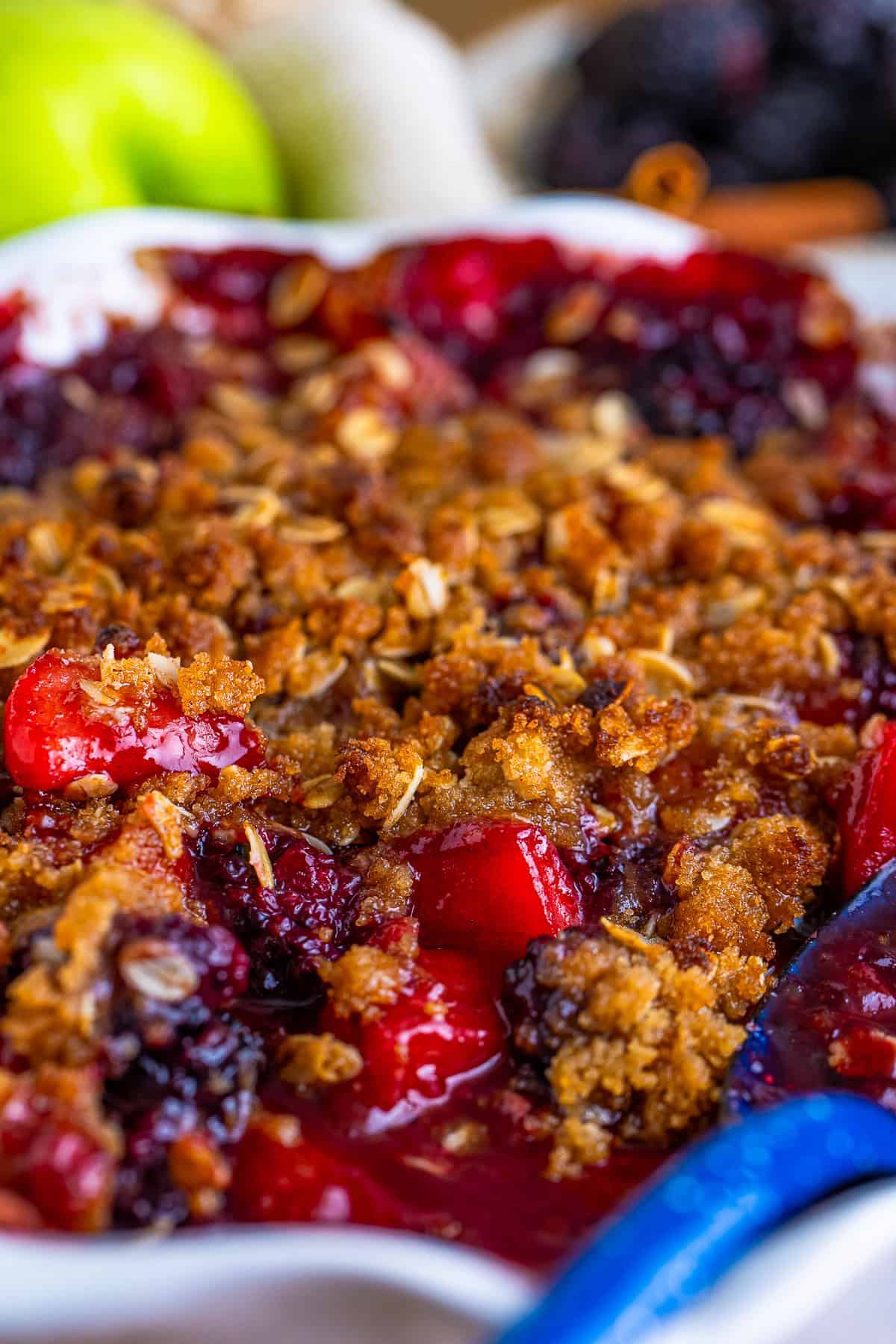 A baking dish of golden apple and blackberry crumble with a crisp oat topping over bubbling fruit.