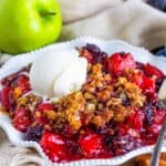 A serving of apple and blackberry crumble topped with a scoop of vanilla ice cream in a white bowl.