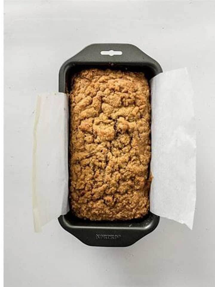 Baked Apple Bread with golden crumble topping in a parchment lined loaf pan.