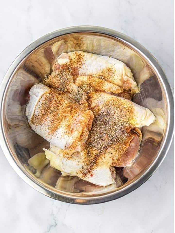 Chicken thighs in a metal bowl with salt, pepper, garlic powder, onion powder, and paprika added.