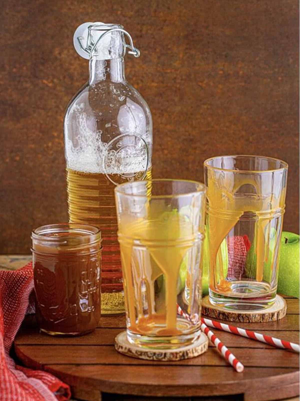 Caramel sauce drizzled inside two tall glasses for an apple cider float.