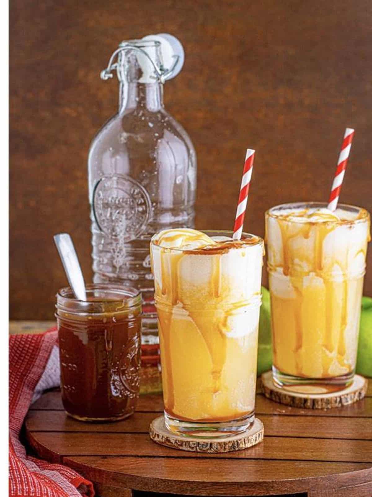 Finished apple cider floats topped with a final caramel drizzle and striped straws.