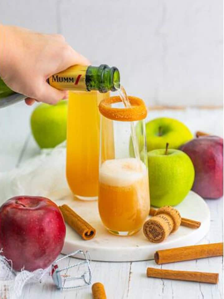 Champagne being poured over chilled apple cider in rimmed flutes.