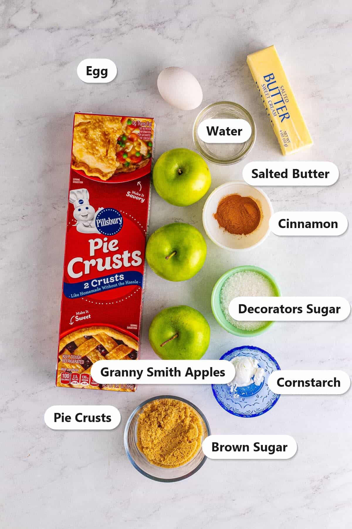 Labeled ingredients for Apple Hand Pies including Granny Smith apples, pie crusts, butter, brown sugar, cinnamon, cornstarch, egg, water, and decorators sugar.