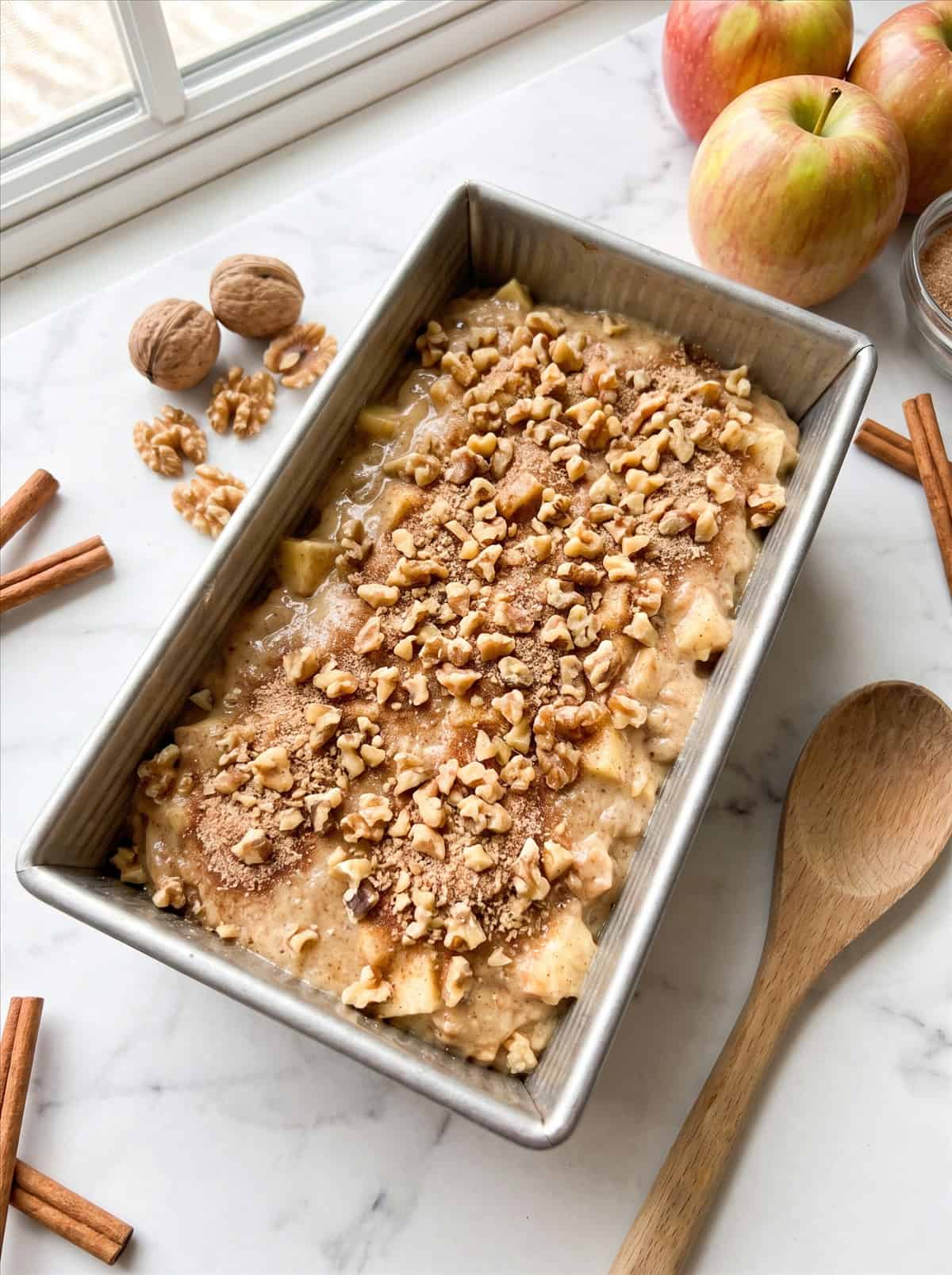 Apple walnut bread batter in a metal loaf pan sprinkled with the cinnamon sugar walnut topping before baking.
