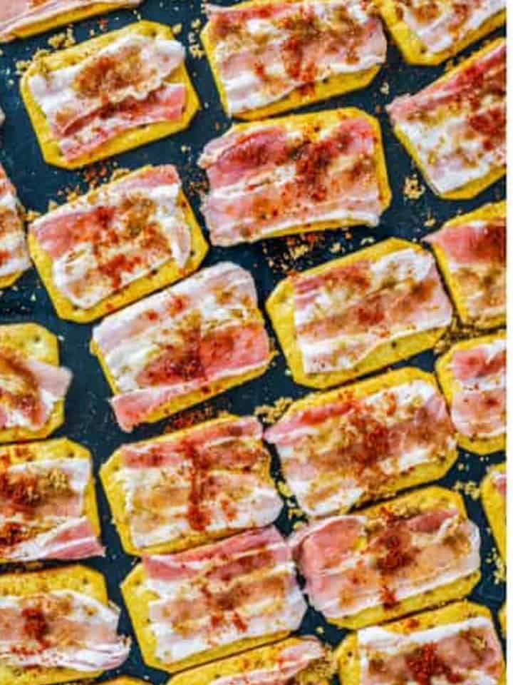 Crackers topped with bacon pieces, brown sugar, and chipotle powder on a wire rack over a sheet tray.