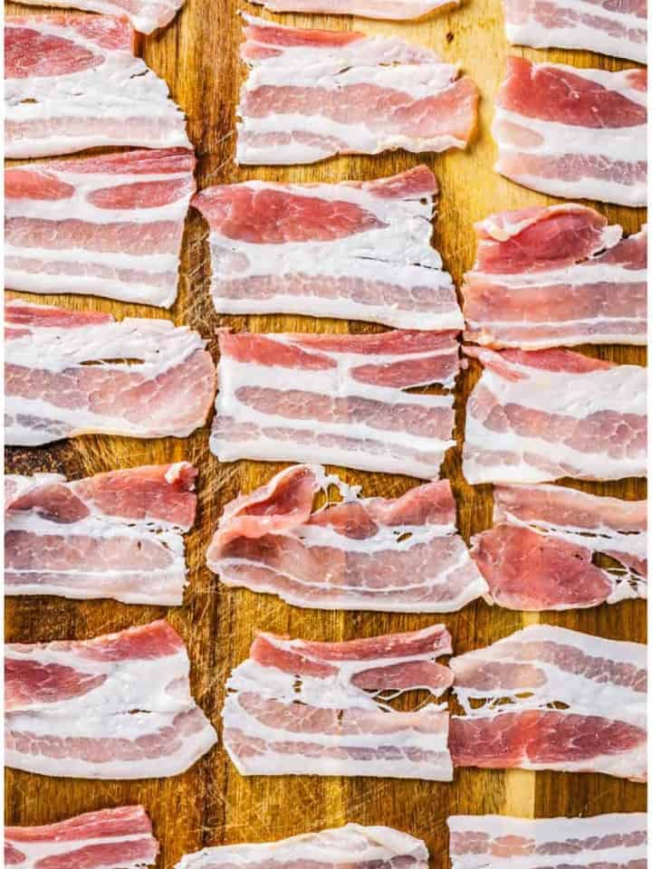 Bacon slices cut into fourths laid out on a wooden cutting board for Bacon Crackers.