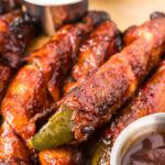 A platter of crispy air fryer Bacon Wrapped Pickles glazed with BBQ sauce and served with ranch dressing.