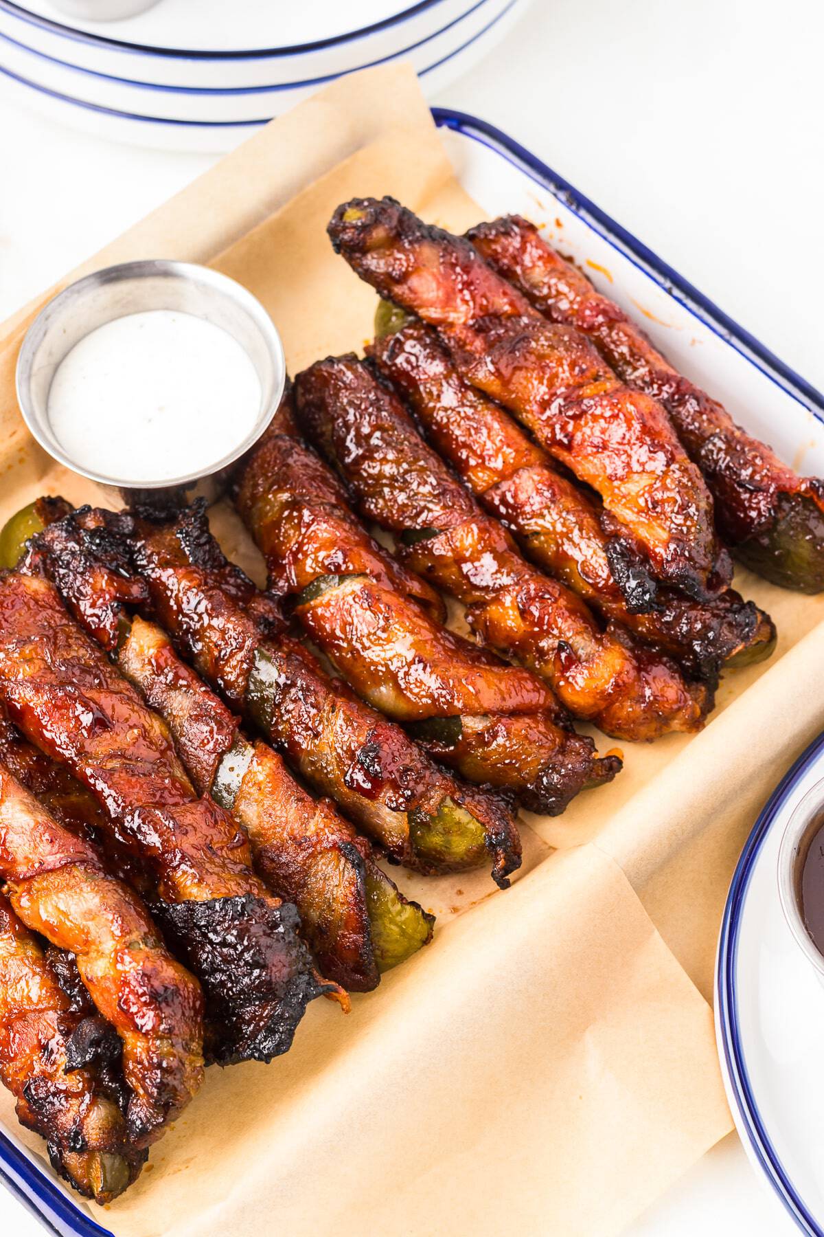 Bacon Wrapped Pickles piled on a board with BBQ sauce and ranch for dipping.