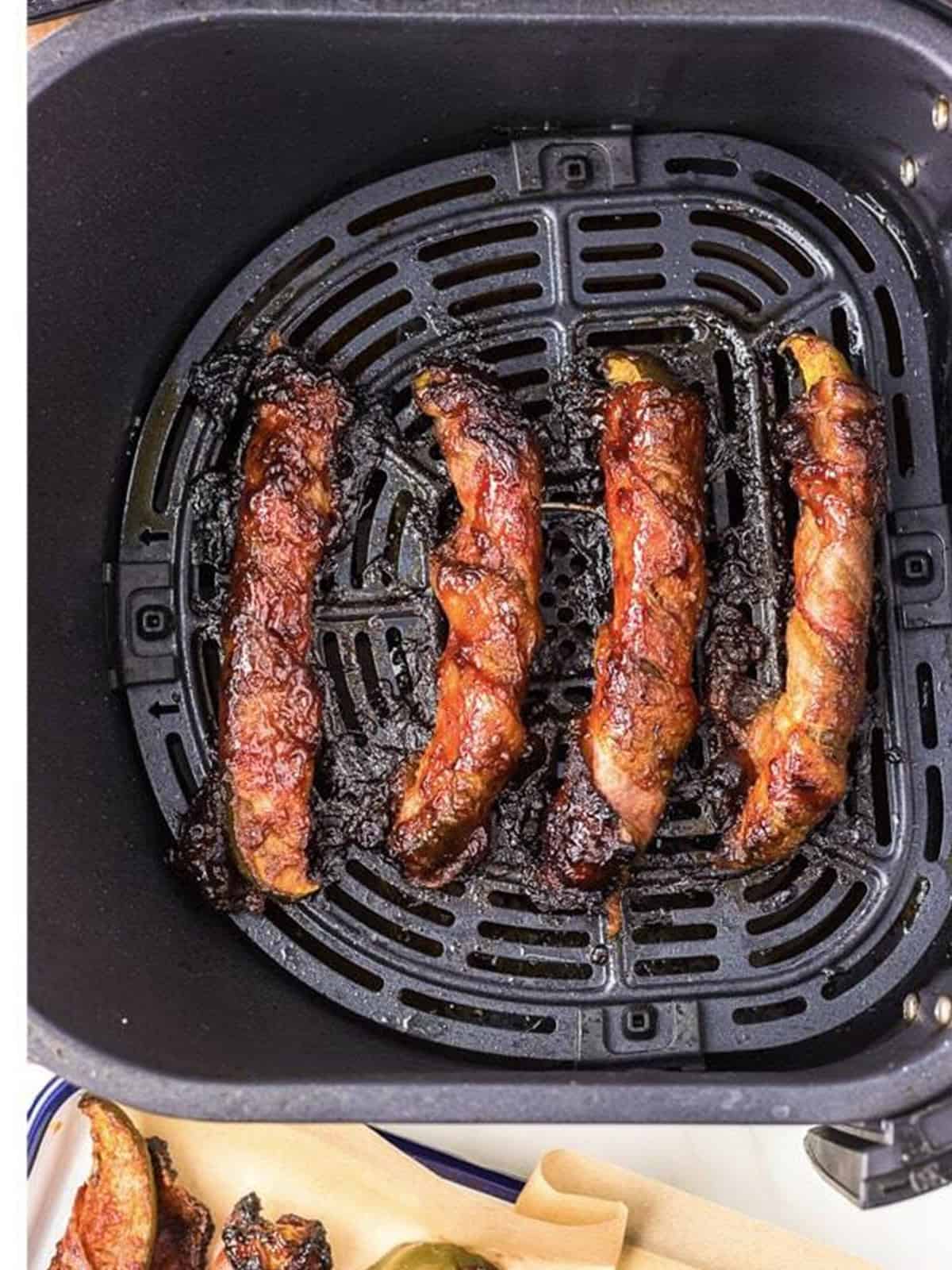 Bacon wrapped pickles arranged in an air fryer basket to cook until crispy.
