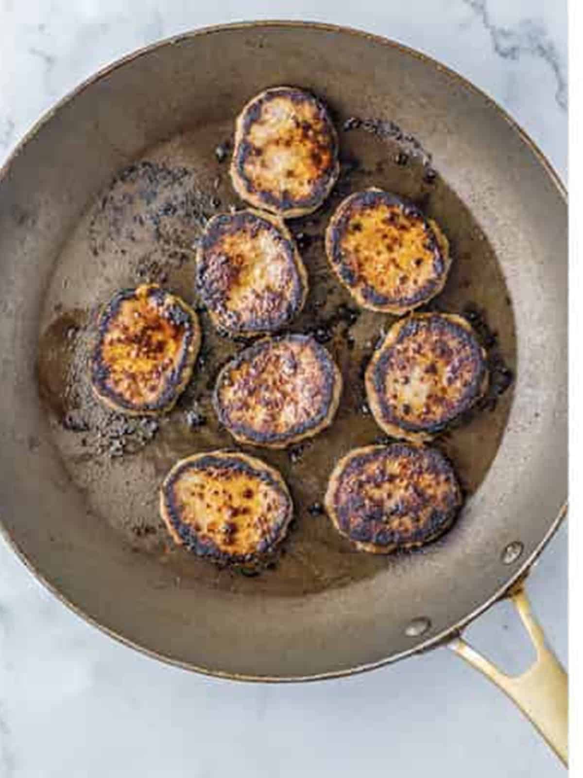 Sausage patties browning in a skillet for bagel breakfast sliders.