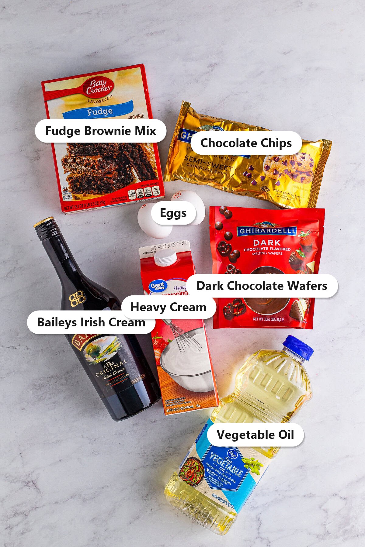 Labeled ingredients for baileys brownies including fudge brownie mix, Baileys Irish Cream, eggs, vegetable oil, chocolate chips, heavy cream, and dark chocolate wafers.