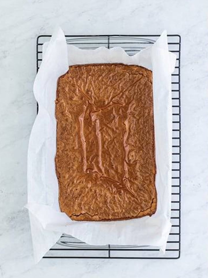 Baked baileys brownie slab cooling on a wire rack in the parchment.