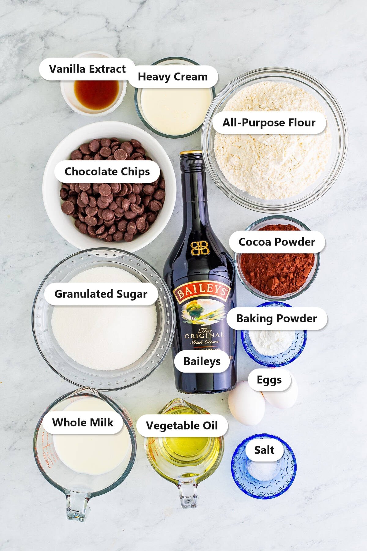 Labeled ingredients for baileys cupcakes including flour, cocoa powder, sugar, milk, oil, eggs, vanilla, Baileys, chocolate chips, heavy cream, baking powder, and salt.