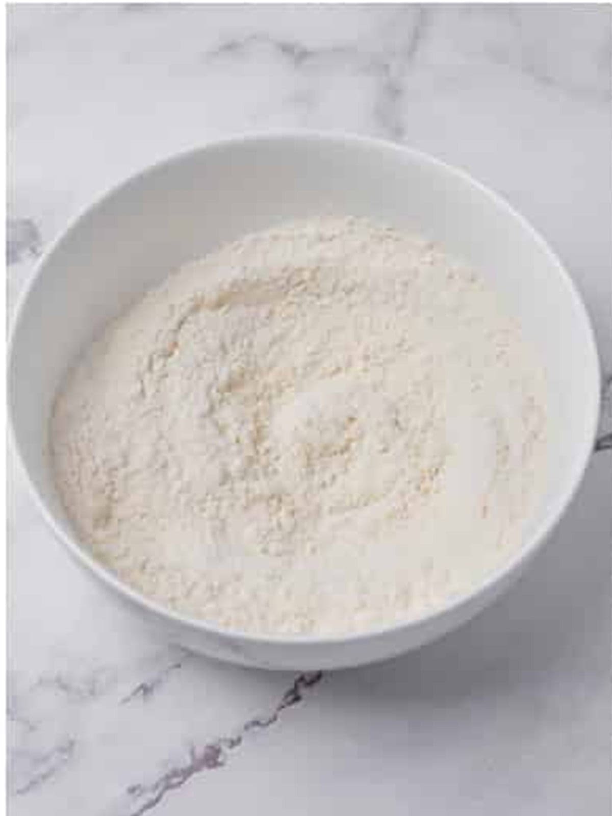 Flour, baking powder, and salt whisked together in a white bowl for baked donut holes.