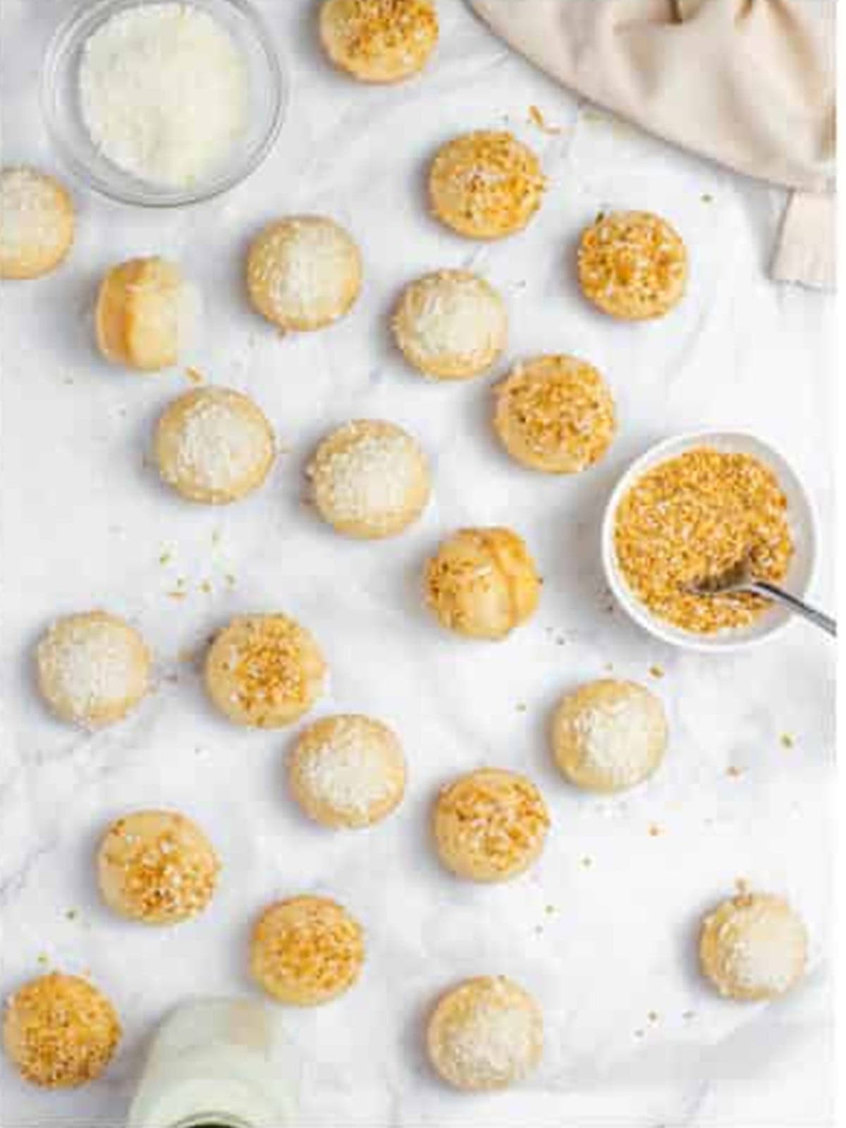 Glazed donut holes topped with toasted and shredded coconut setting on parchment.