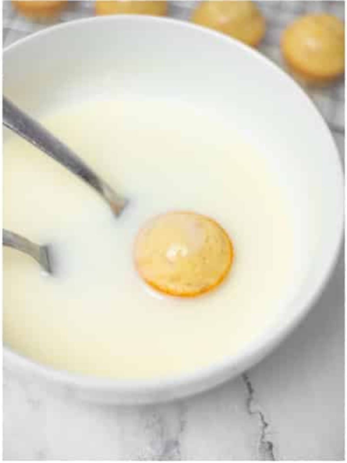 A baked donut hole being dipped into vanilla glaze with two forks.