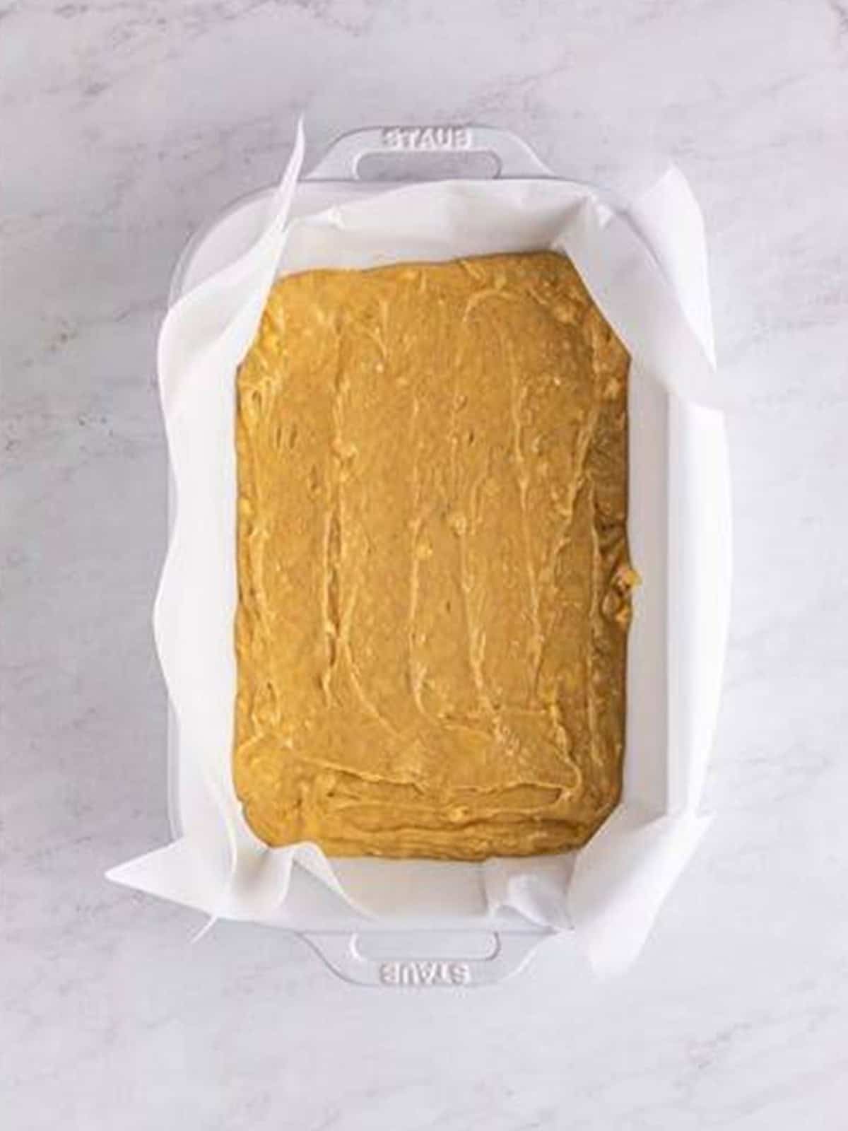 Banana Blondies batter spread evenly in a parchment lined baking dish.