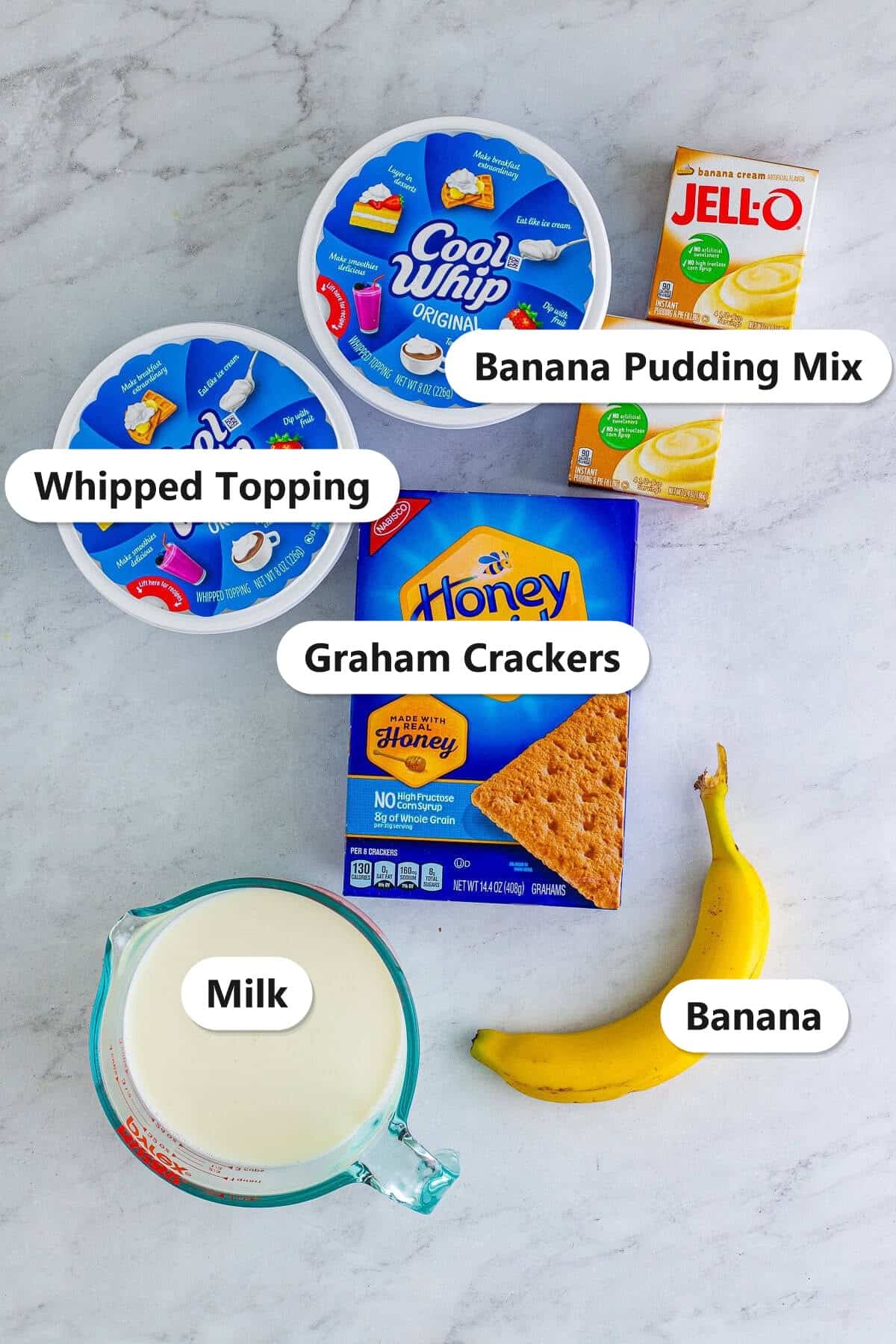 Labeled ingredients to make banana icebox cake including banana pudding mix, whipped topping, graham crackers, milk, and a banana.