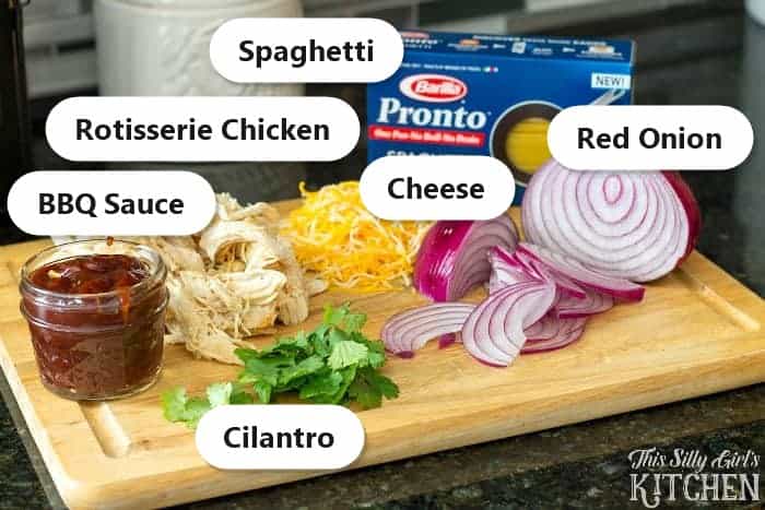 Labeled ingredients to make BBQ chicken pasta including spaghetti, rotisserie chicken, BBQ sauce, cheese, red onion, and cilantro