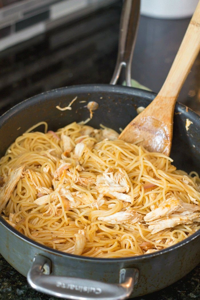 One pan BBQ chicken pasta simmering in a skillet with a wooden spoon
