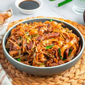 A bowl of Beef Chow Ho Fun with wide rice noodles, seared flank steak, and vegetables in a savory soy sauce.