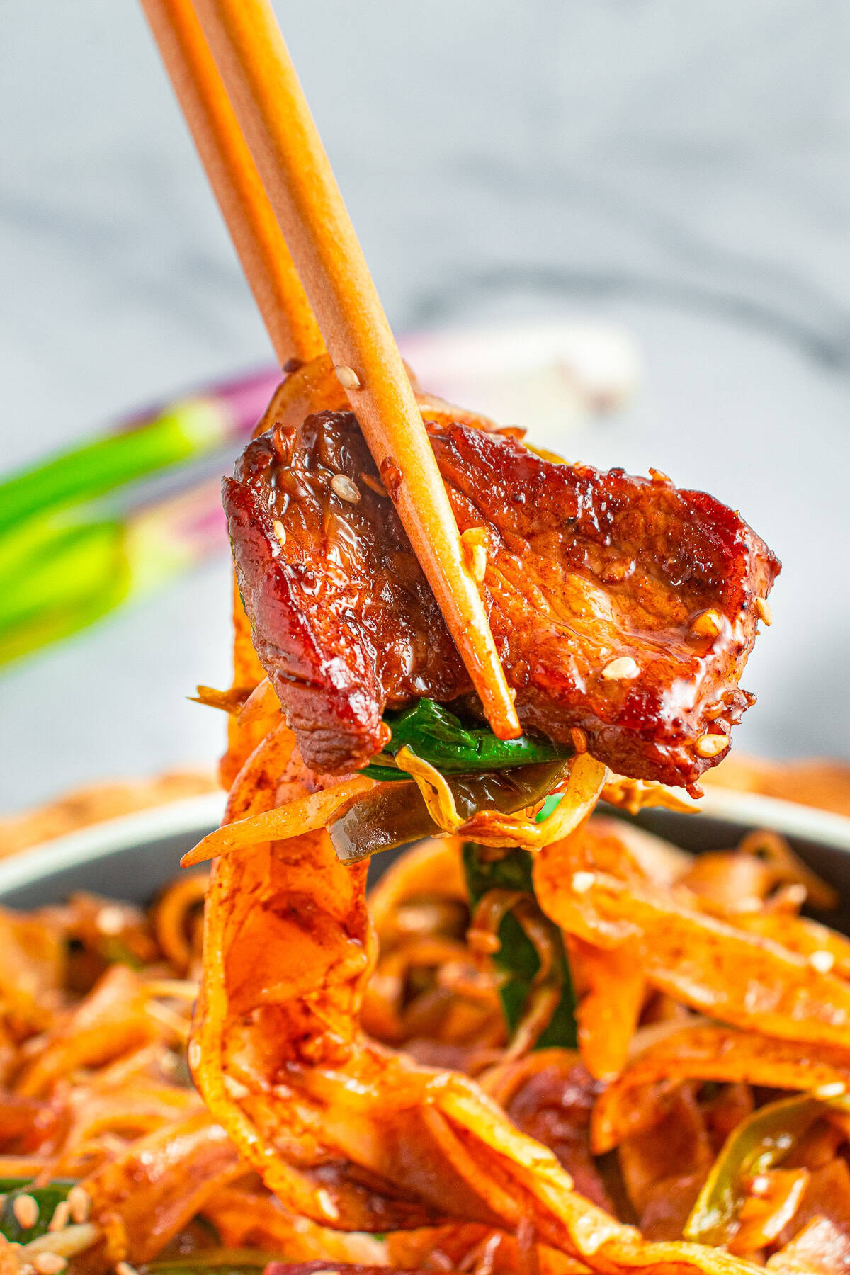 Chopsticks lifting a piece of saucy beef and wide ho fun noodles from a bowl of Beef Chow Ho Fun.