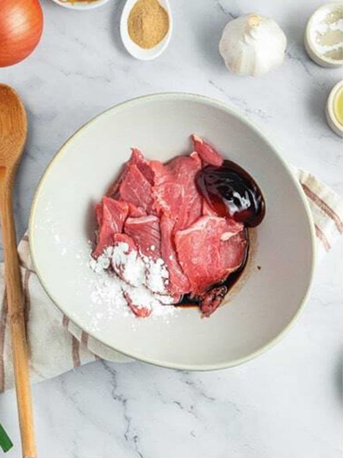 Sliced flank steak in a bowl with soy sauce, oyster sauce, cornstarch, and sesame oil to marinate for Beef Chow Ho Fun.