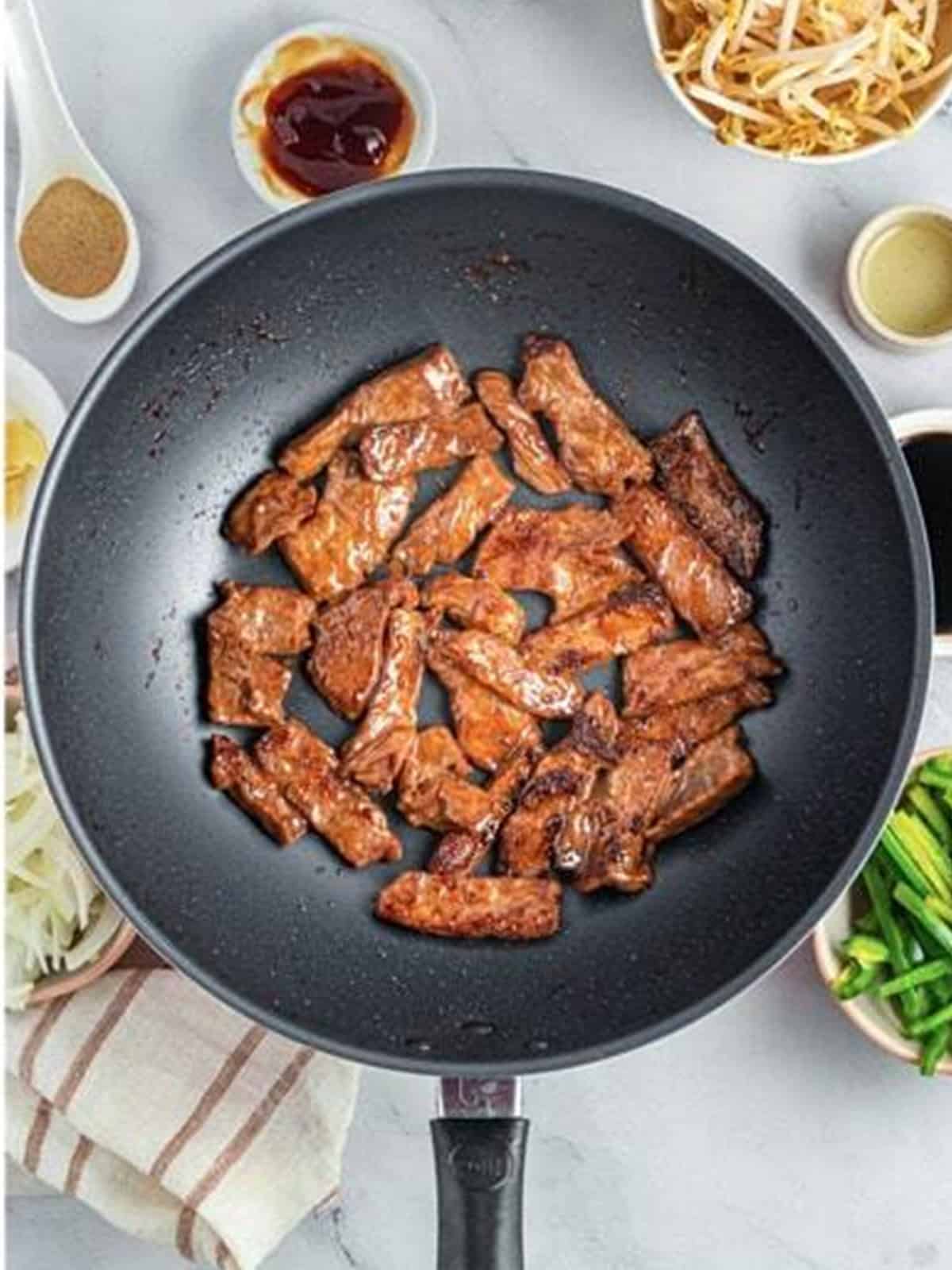 Marinated beef strips stir-frying in a hot wok until just cooked for Beef Chow Ho Fun.