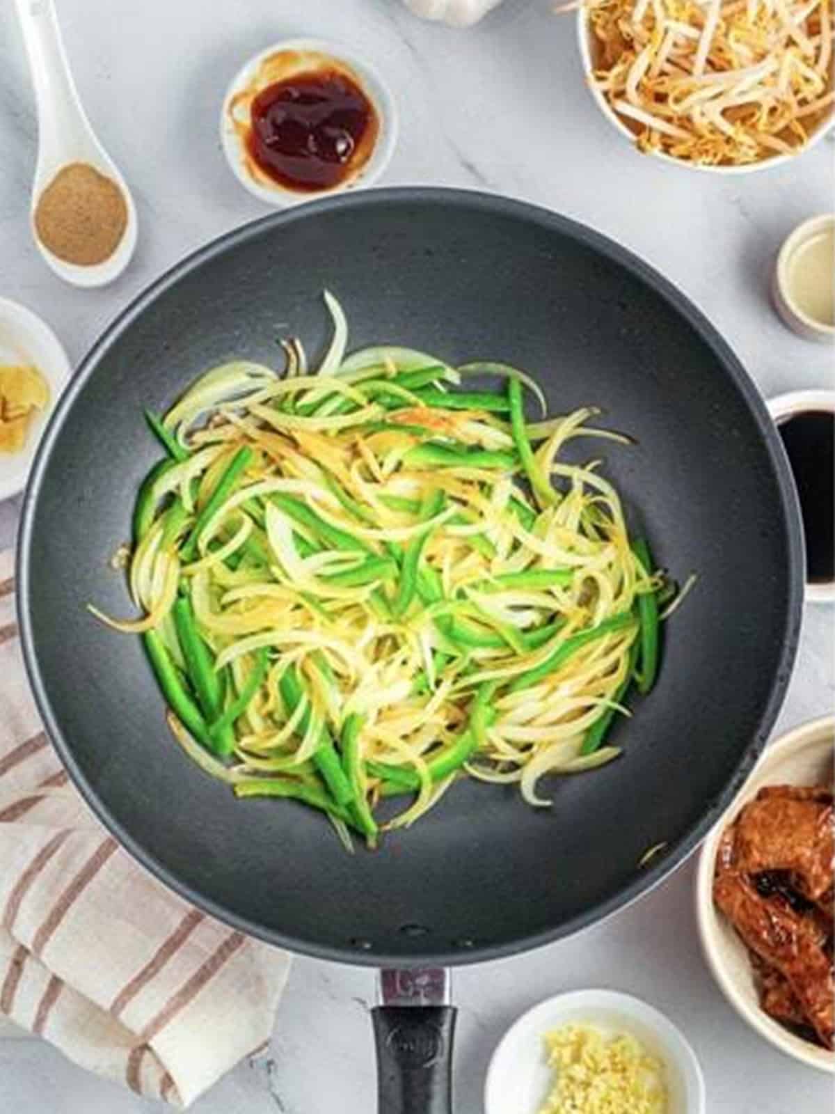 Sliced onion and green bell pepper stir-frying in a wok for Beef Chow Ho Fun.