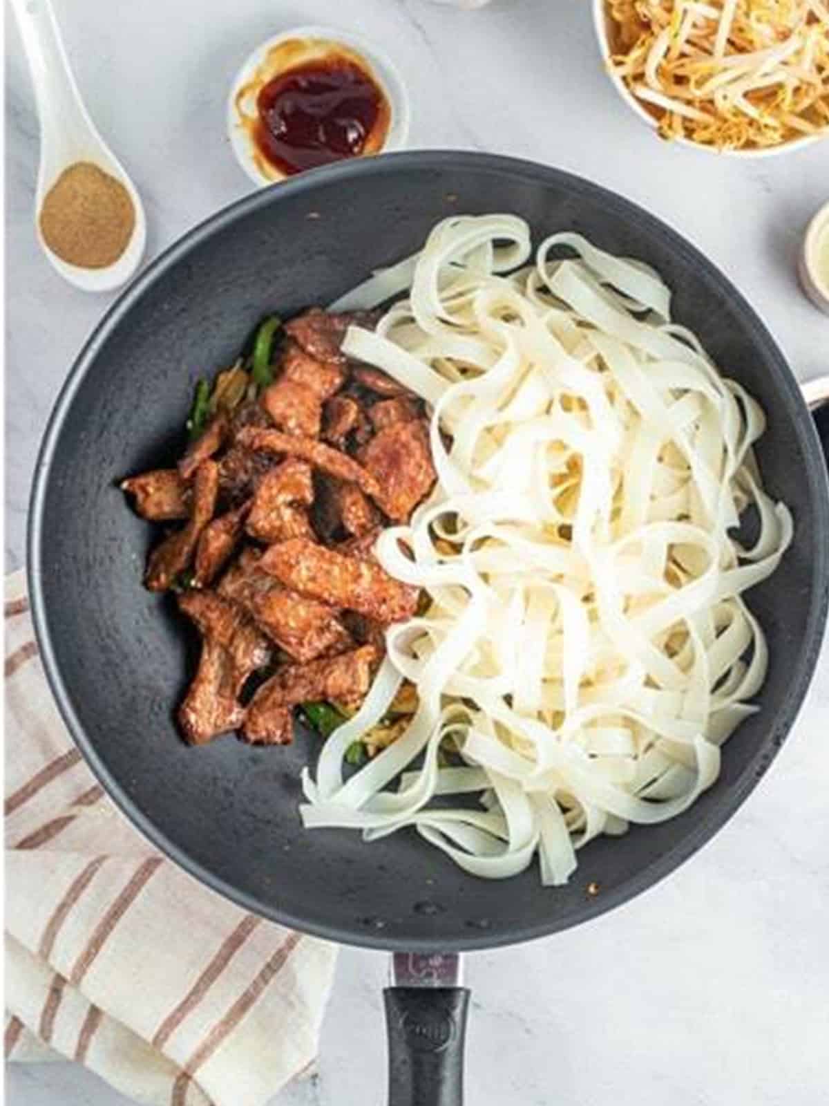 Wide ho fun noodles and seared beef added to the wok of vegetables for Beef Chow Ho Fun.