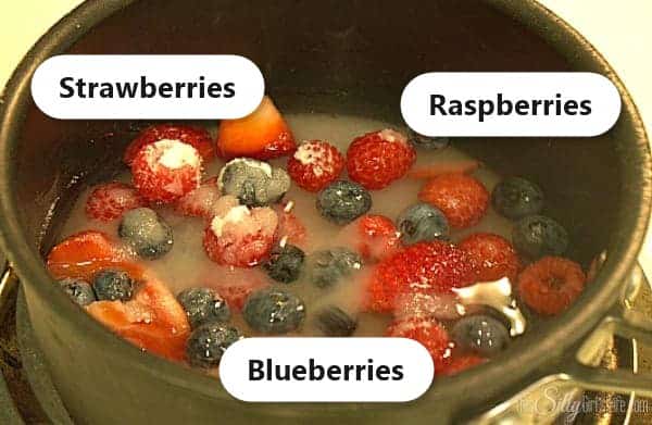 Strawberries, blueberries, and raspberries labeled in a pot with sugar and water for berry simple syrup.