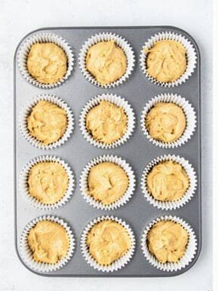 Biscoff cupcake batter divided between liners in a cupcake pan.