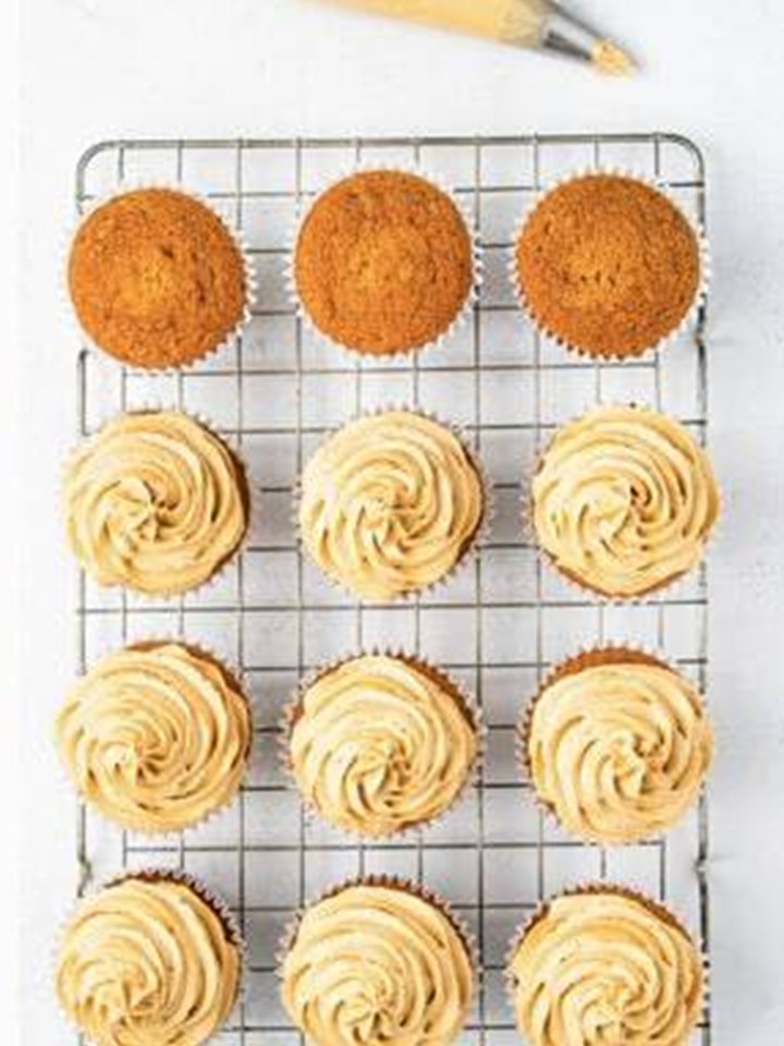 Baked Biscoff cupcakes with piped cookie butter frosting swirls on a wire rack.