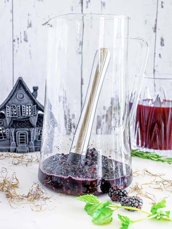 Blackberries and agave nectar muddled in the bottom of a glass pitcher.