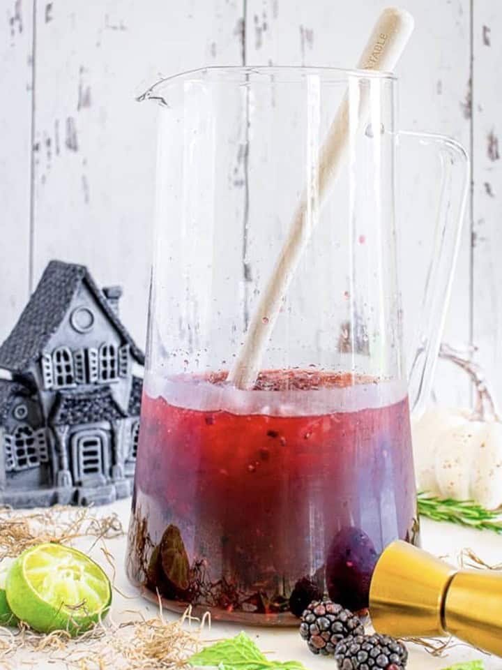 The blackberry margarita stirred together in a glass pitcher with a wooden spoon.